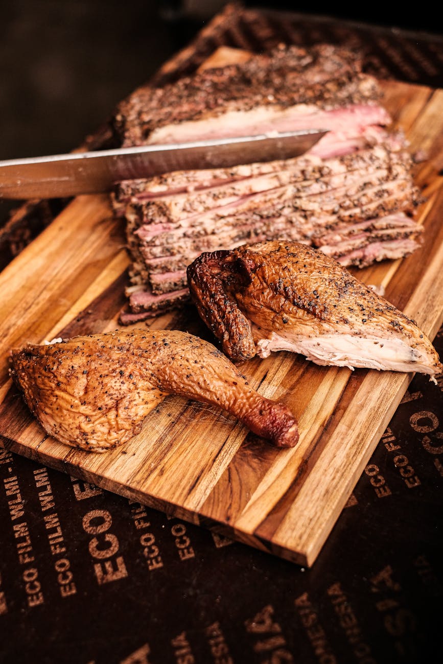 A whole smoked brisket and chicken leg on a wood cutting board, mid-slice.