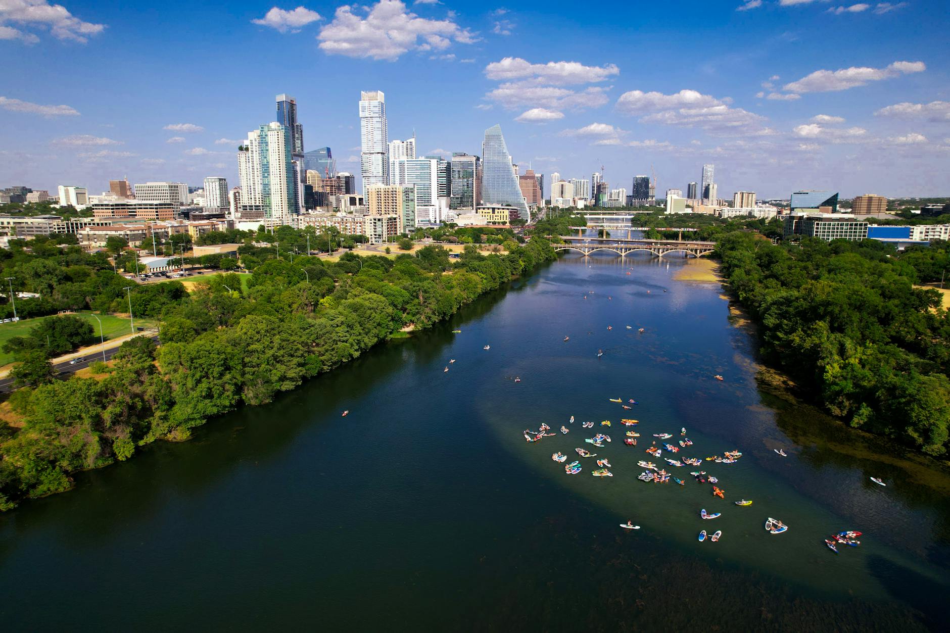 Aerial view of paddleboarders and kayakers on Lady Bird Lake with the downtown Austin skyline behind.