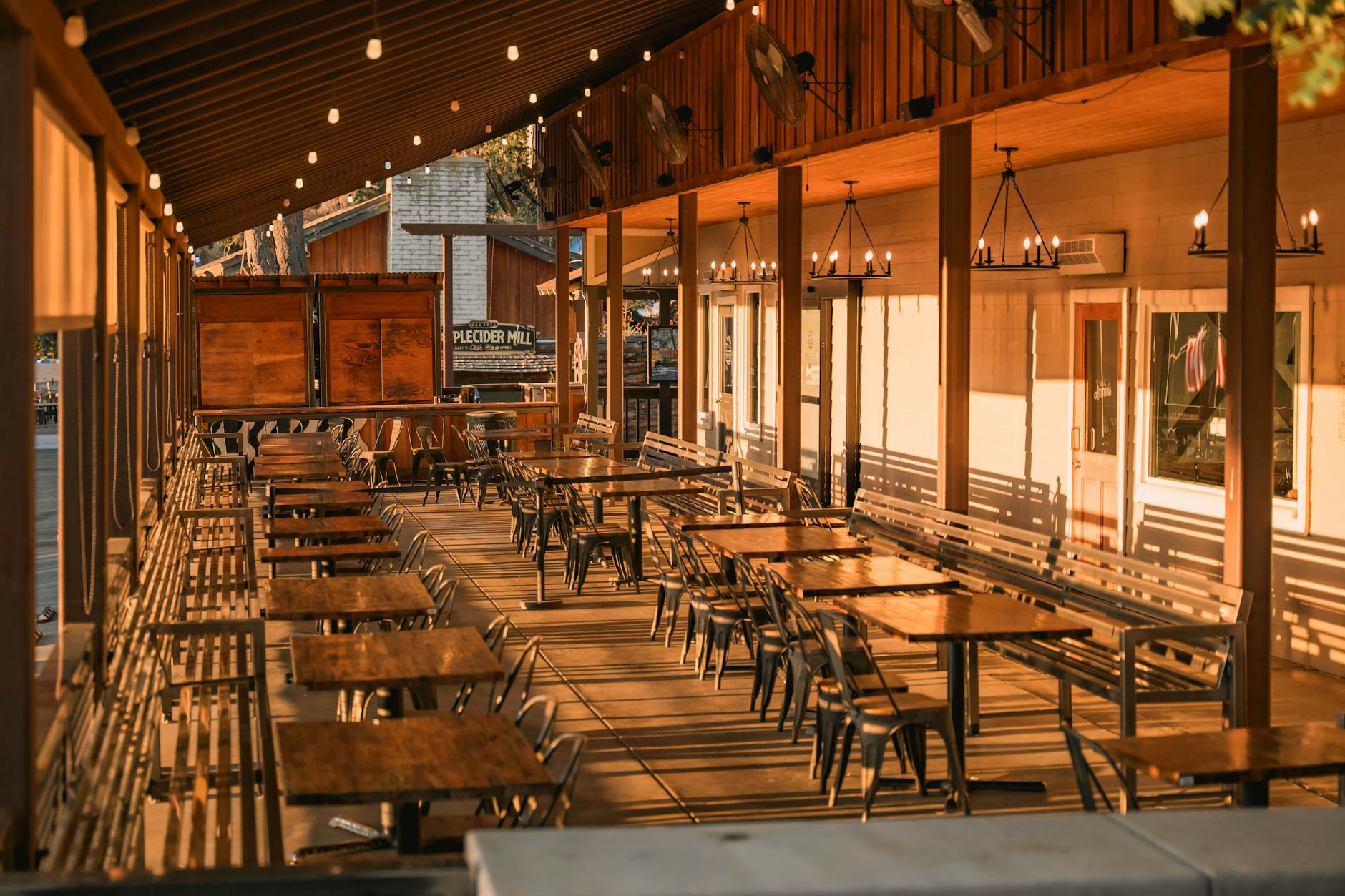 A long warmly lit wood patio of a bar at dusk, string lights overhead, ready for the evening.