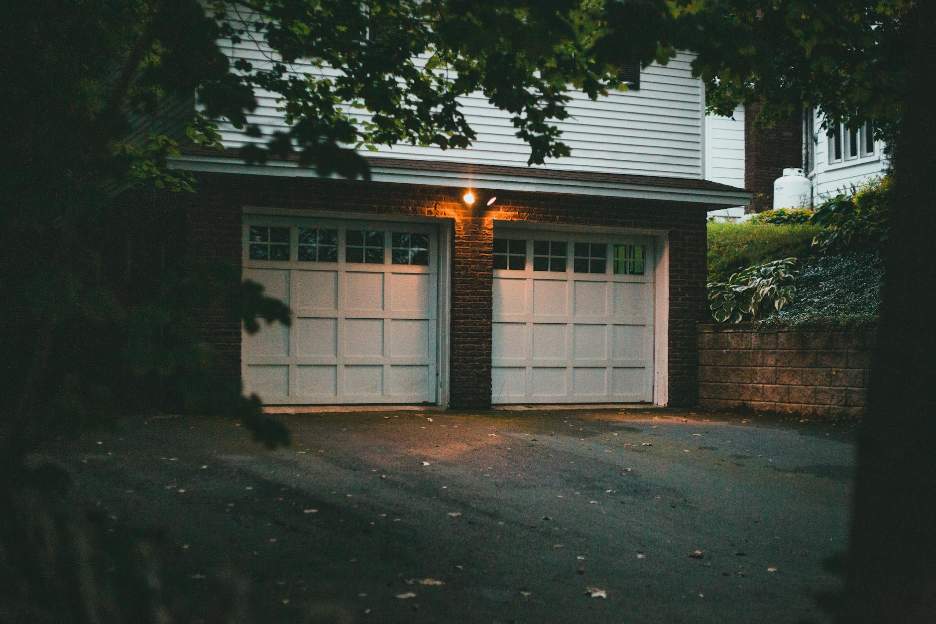 A quiet suburban two-car garage in dim evening light, a single porch lamp on.