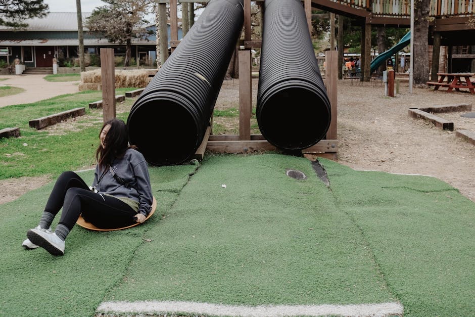 A person at a playground in Austin, Texas, with a tube slide and surrounding park structures.
