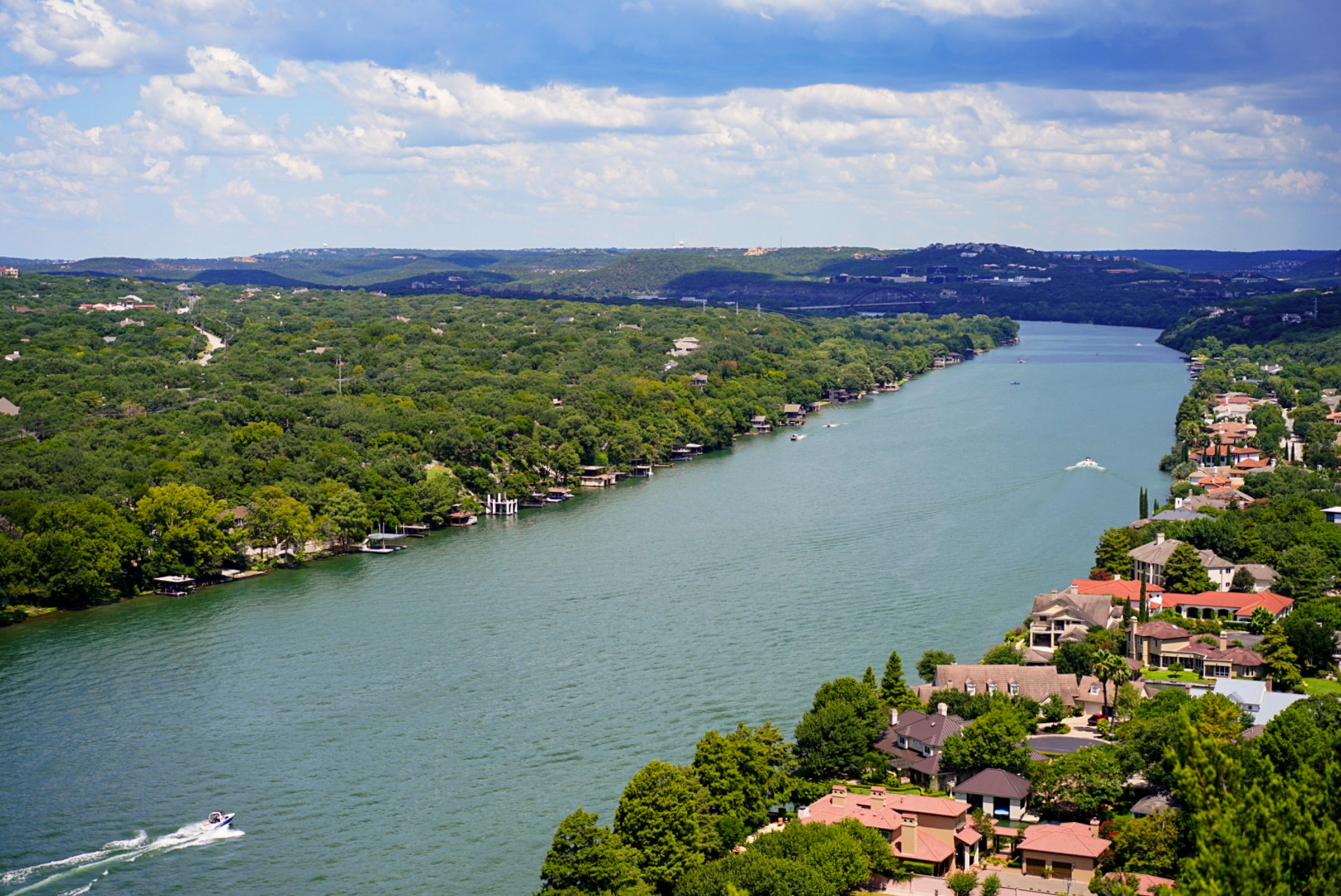 An aerial view of Lake Austin homes along a tree-lined shoreline, in the Westlake / Eanes ISD area.